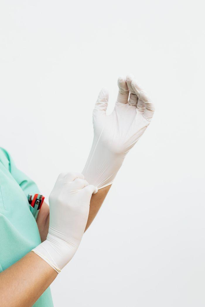 A healthcare worker in green scrubs wearing white surgical gloves, preparing for procedure.