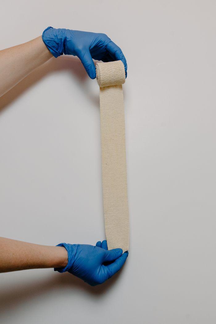 Hands in blue gloves roll a gauze bandage for medical use.